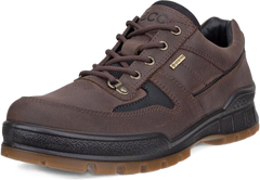 A dark brown leather lace-up shoe with black accents, a small gold-tone metal badge on the side, and a brown outsole, shown against a plain white background.
