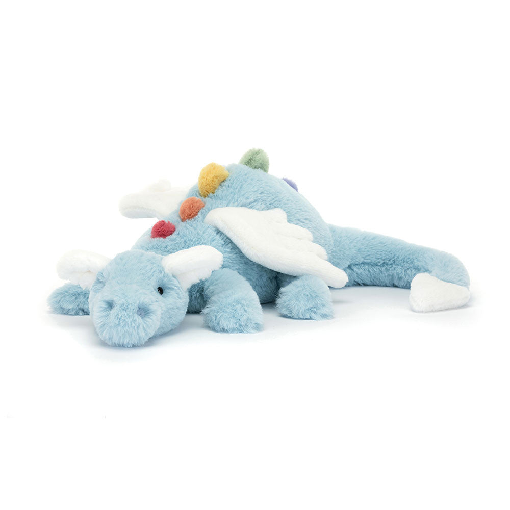 A large plush toy resembling a dragon with a sky-blue body, white wings, and a multi-colored rainbow spine.